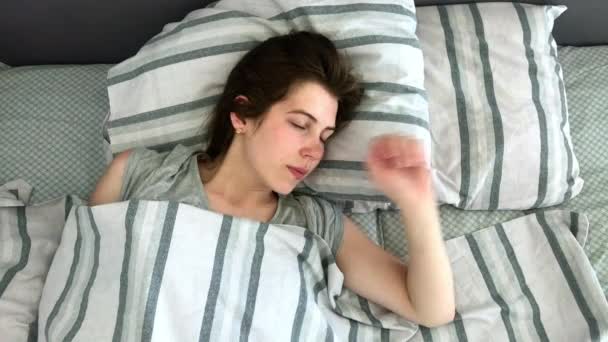 美しい若いブルネットは、朝の早い時間に彼女のベッドで魅力的に眠ります。静かに眠る少女の甘くて温かい眺め - 映像、動画