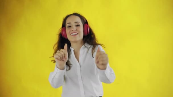 Young attractive woman listens to music with headphones and smiles in Studio with yellow Background. - Imágenes, Vídeo
