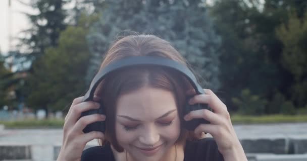 Urban lifestyle: young attractive brown-haired woman puts on wireless headphones and smiles - Filmati, video