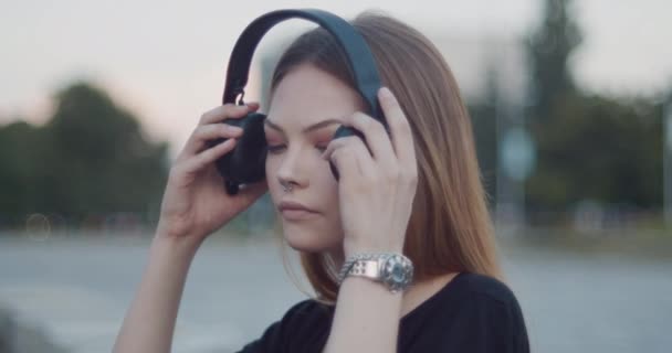 Kaunis ruskeahiuksinen tyttö kuuntelee musiikkia suurilla mustilla bluetooth-kuulokkeilla
 - Materiaali, video