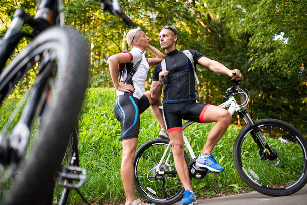Athlétisme homme et femme avec des vélos posant dans le parc sur un fond de monticule vert
. - Photo, image
