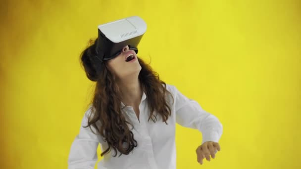 Happy young woman with virtual reality headset or 3d glasses on yellow background at studio. - Footage, Video