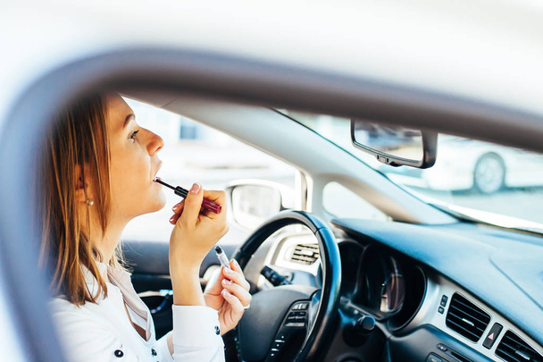 Business Woman paints lips in a car - Foto, afbeelding