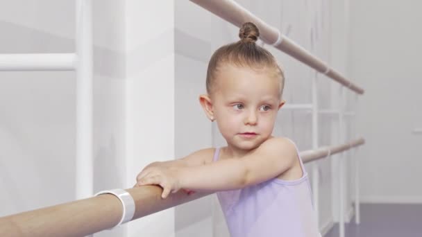 Αξιολάτρευτο μικρό μπαλαρίνα κορίτσι βάζοντας το πόδι της σε μπαρ μπαλέτου για τέντωμα - Πλάνα, βίντεο