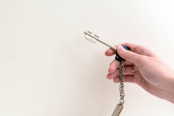 em uma mão feminina uma chave metálica em um fundo branco. Conceito - habitação de aluguel, hipoteca
 - Foto, Imagem