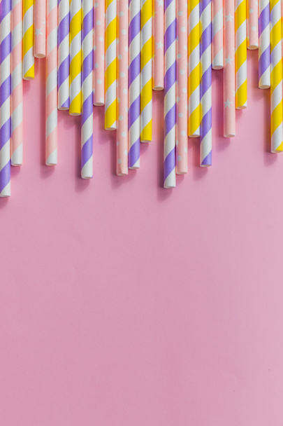 Paper straw of pastel colors on pink background. Many cocktail straws with pink, yellow and purple stripes.refusal of disposable plastic drinking straw in favor of reusable paper drinking straw. - Foto, imagen