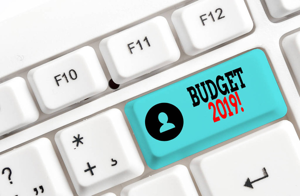 予算2019を示す概念的な手書き。ビジネス写真は、白い背景の上にノート紙と今年のホワイトPCキーボードの収入と支出の見積もりを示しています. - 写真・画像