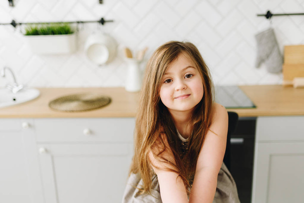 Porträt eines süßen kleinen kaukasischen Mädchens, das in der Küche sitzt und lächelt - Foto, Bild