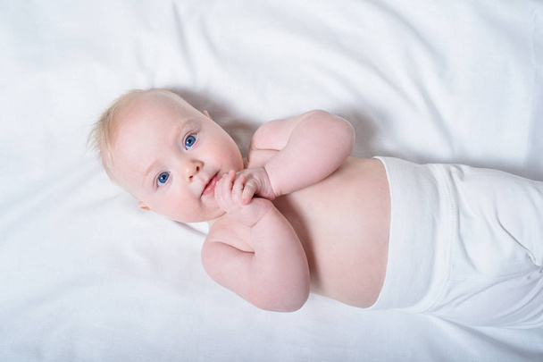Lindo bebé rubio con un torso desnudo acostado en sábanas blancas. Vista superior
 - Foto, imagen