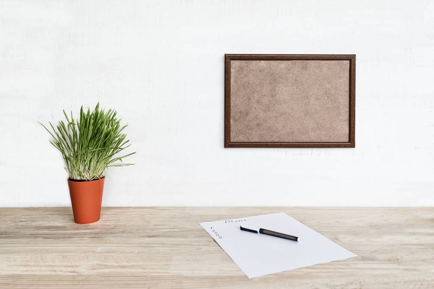 Leeg frame op witte muur. Vel papier en een pen, groene kamerplant op de tafel. Werkruimte thuis - Foto, afbeelding