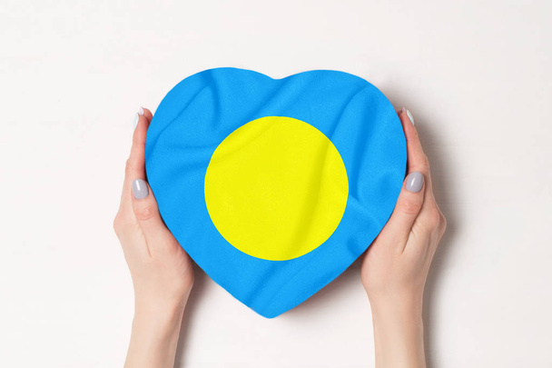 Flaga Palau na polu w kształcie serca w kobiecych rękach. Białe tło - Zdjęcie, obraz