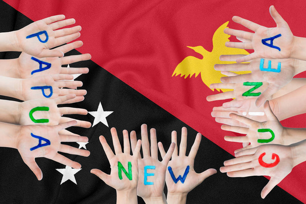 Papua Yeni Gine'nin sallanan bayrağının arka planına karşı çocukların ellerindeki Papua Yeni Gine yazıtı - Fotoğraf, Görsel
