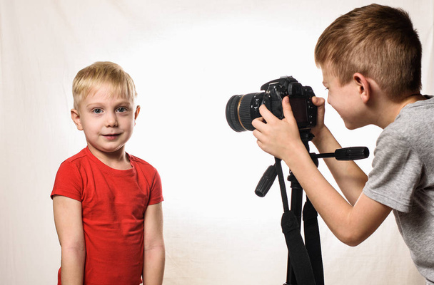 Το μικρό ξανθό αγόρι είναι έτοιμο να δώσει τη συνέντευξη, το αγόρι το παίρνει στην βιντεοκάμερα. Νέος blogger βίντεο. Λευκό φόντο - Φωτογραφία, εικόνα