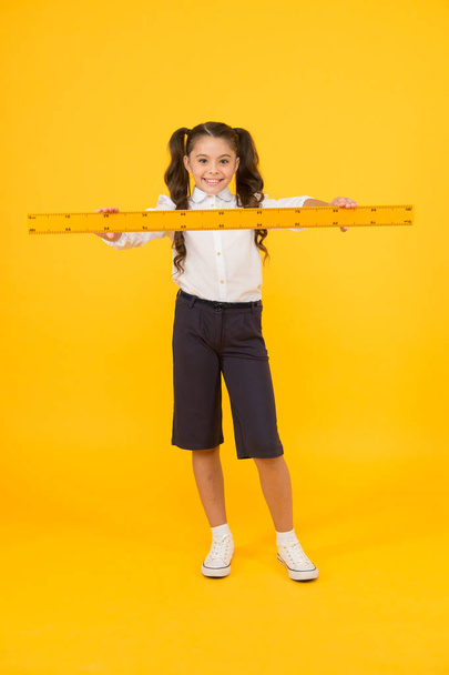 Studying is fun. School adorable student study geometry. Kid school uniform hold ruler. Pupil cute girl with big ruler. Geometry school subject. Education and school concept. Sizing and measuring - Photo, image