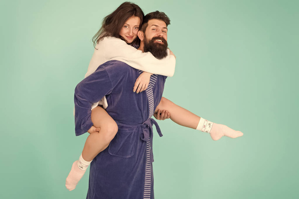 Lets stay at home and have fun. Couple in bathrobes having fun turquoise background. They always have fun together. Close relationship. Handsome young man giving his girlfriend piggyback ride - Фото, зображення
