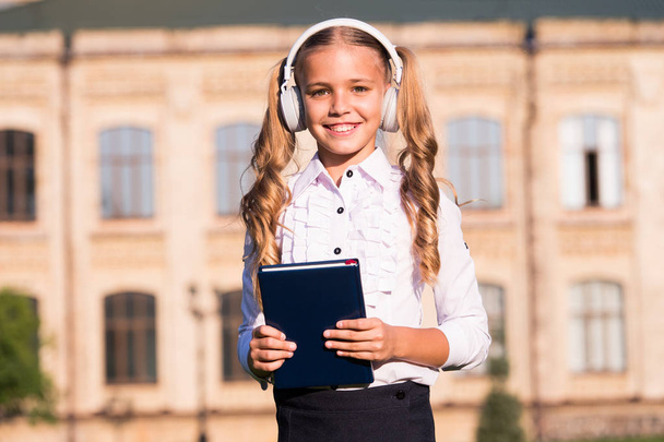 Listening school book. Digital technologies for learning. Elearning and modern methods. Girl cute schoolgirl hold book and headphones. Knowledge assimilate better this way. Audio book concept - Fotografie, Obrázek