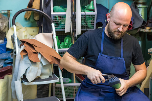 Retrato de un zapatero trabajando sobre una suela, doblando clavos con un alicate de zapatos sentado en su taller
. - Foto, Imagen