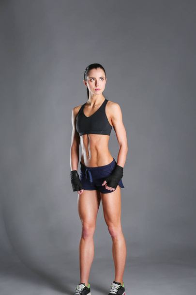 muskulöse junge Frau posiert in Sportbekleidung vor schwarzem Hintergrund. - Foto, Bild