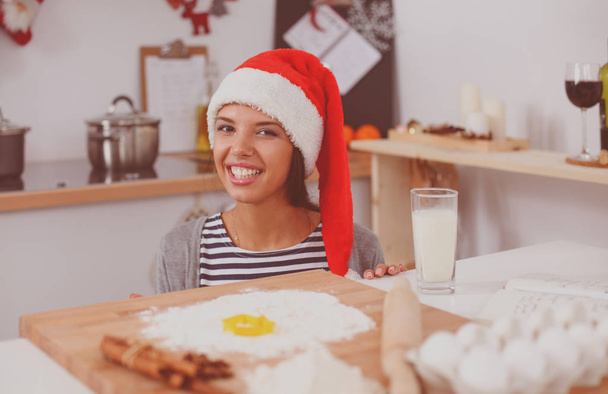 Télapó kalapos nő karácsonyi sütiket süt a konyhában - Fotó, kép