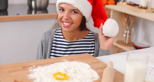 Woman in santa hat making christmas cookies in the kitchen - Fotó, kép