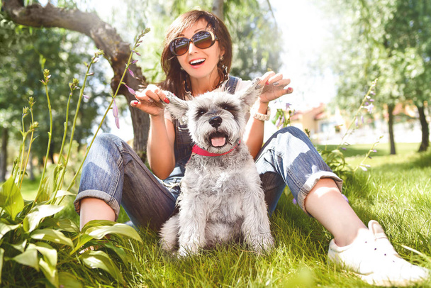 mujer caucásica feliz en gafas de sol descansando en la naturaleza con su amado perro schnauzer. concepto de amor por los animales. mejores amigos
 - Foto, imagen