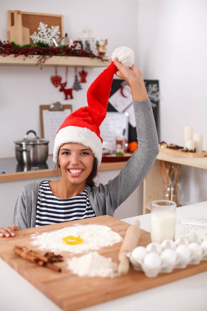 Woman in santa hat making christmas cookies in the kitchen - Foto, afbeelding