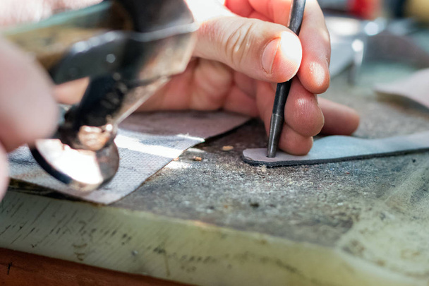 男性の靴職人の手は、パンチで革の一部に穴を作ります. - 写真・画像