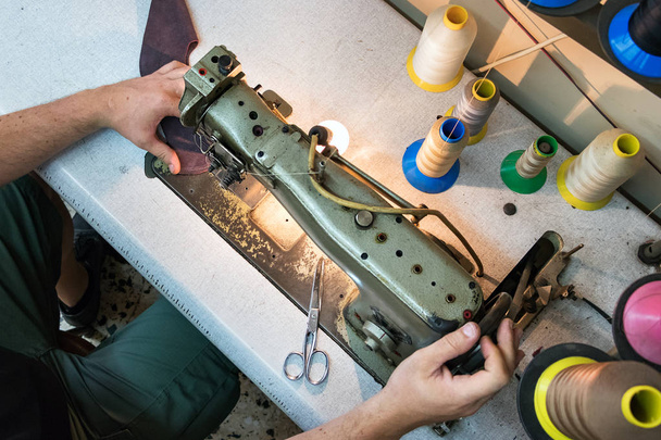 Vista superior de un zapatero masculino cosiendo cuero con una vieja máquina de coser
. - Foto, Imagen