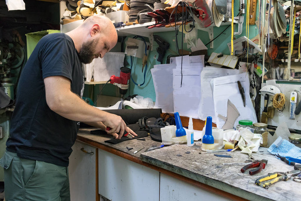 Een mannelijke schoenmaker snijden met een frees op een rubberen zool om een sandaal te repareren in zijn werkplaats. - Foto, afbeelding