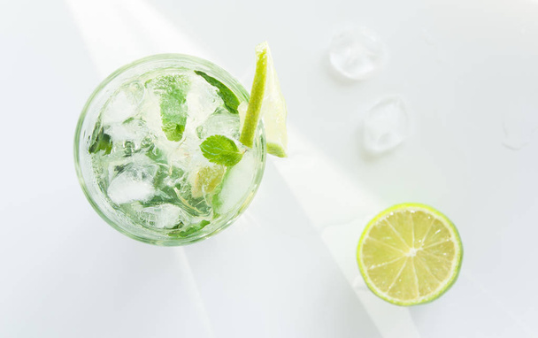 Mojito cocktail in een transparant glas met ijs. Recept voor exotische dranken met munt, limoen en witte rum. Glas met een cocktail op een witte achtergrond in de zonnestralen. - Foto, afbeelding