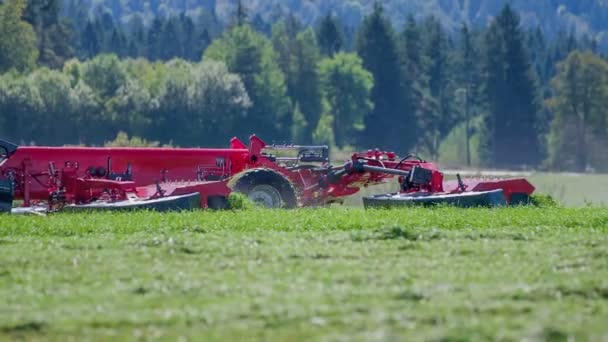 Een boer rijdt zijn tractor en trekt een Landbouwmachine achter zich. De boeren snijden gras. - Video
