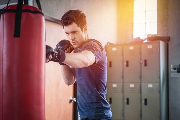Handsome man in boxing gloves punching bags exercise in fitness  - Photo, Image
