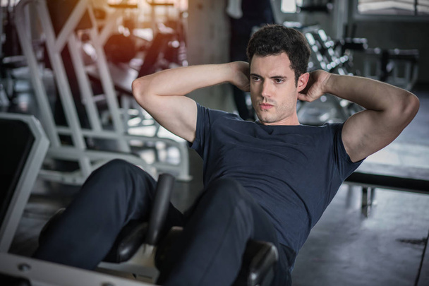 Przystojny człowiek ćwiczenia robi siedzieć w górę brzucha ćwiczenia w siłowni - Zdjęcie, obraz