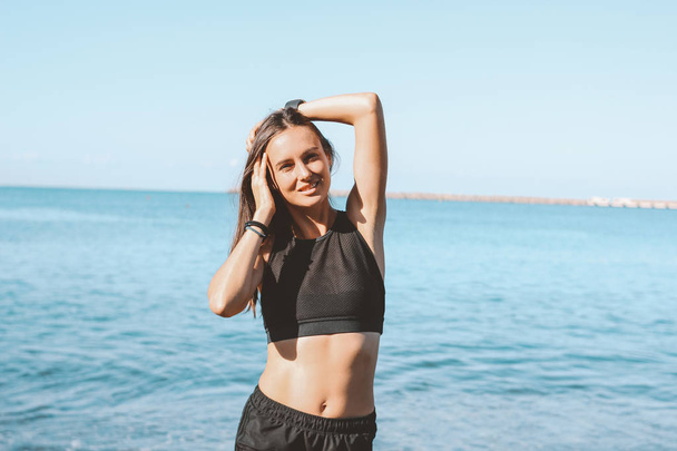 junge schlanke athletische lange Haare lächelnde Frau in Sportbekleidung am Meeresstrand, gesunder Lebensstil - Foto, Bild