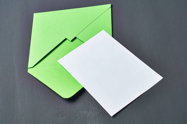 Blank white paper sheet near green opened square envelope lies on old scratched dark concrete. Space for text - Foto, imagen