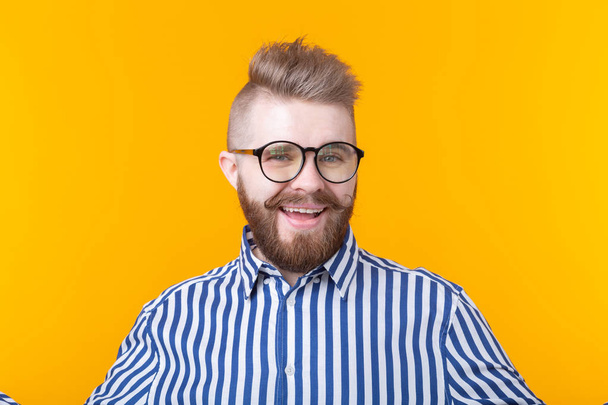 Молодой позитивный хипстер с усатой бородой в рубашке позирует на жёлтом фоне
. - Фото, изображение