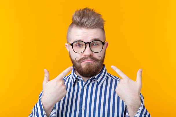 Viehättävä luottavainen nuori muoti hipster mies lasit ja parta näyttää itsensä poseeraa keltaisella taustalla. Paikka mainontaan. Itseluottamuksen ja menestyksen käsite
. - Valokuva, kuva