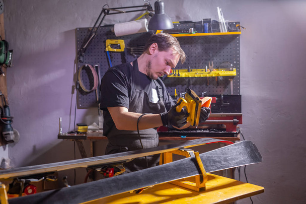 A man in work clothes repairman in the workshop ski service repairing the ski - Fotografie, Obrázek