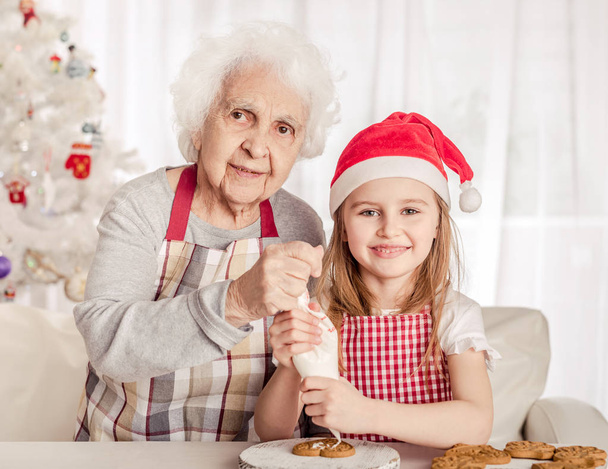 Grandmother with granddaughter holding baked cookie - Fotoğraf, Görsel