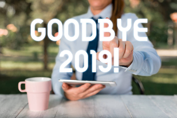 Text sign showing Goodbye 2019. Conceptual photo express good wishes when parting or at the end of last year Female business person sitting by table and holding mobile phone. - Fotó, kép