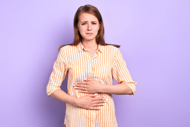 Sad young woman suffers from stomachache, feels discomfort in belly - 写真・画像
