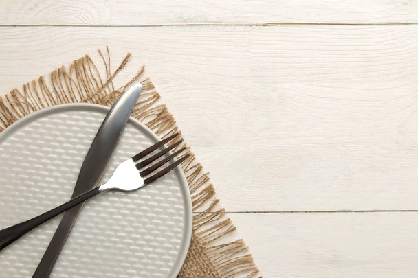 сервировка стола. столовые приборы. Вилка, нож и серая тарелка на белом деревянном столе. вид сверху
 - Фото, изображение