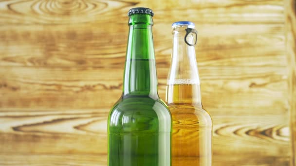 Two beer bottles rotating on wood texture surface. Close up of alcohol drink in transparent and green bottle. - Πλάνα, βίντεο