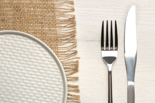 Tischdekoration. Besteck vorhanden. Gabel, Messer und grauer Teller auf einem weißen Holztisch. Ansicht von oben - Foto, Bild