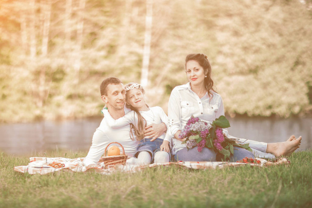 pregnant woman with a bouquet of lilacs and her family sitting on the grass near the river - Foto, immagini