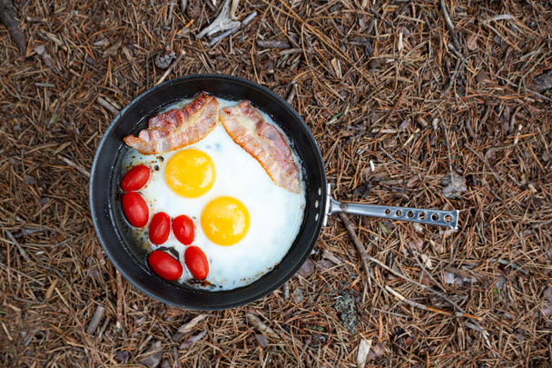 Cuisiner le petit déjeuner sur une cuisinière à gaz dans un camp d'été. Œufs, bacon et tomates sur la casserole
. - Photo, image