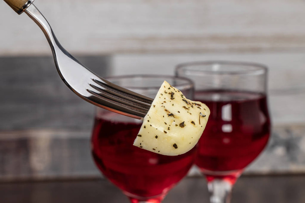 Kousek sýra na vidličce zblízka na pozadí dvou sklenic s červeným vínem - Fotografie, Obrázek