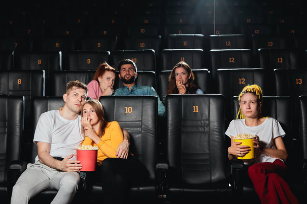映画館に座っている間、おびえたカップルがお互いに寄りかかっている - 写真・画像