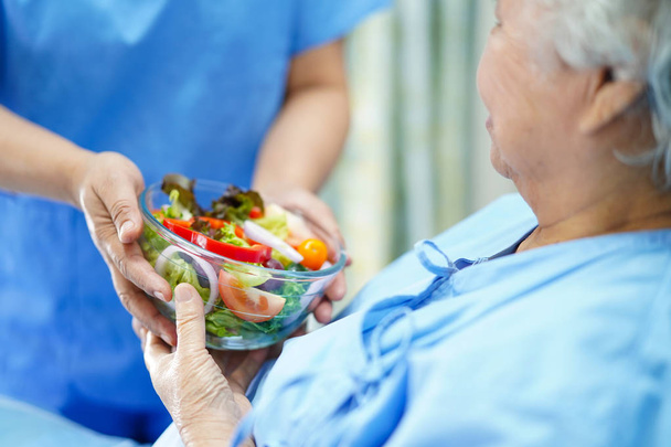 Asiática senior o anciana anciana mujer paciente comiendo desayuno comida saludable con esperanza y feliz mientras está sentada y hambrienta en la cama en el hospital
. - Foto, imagen