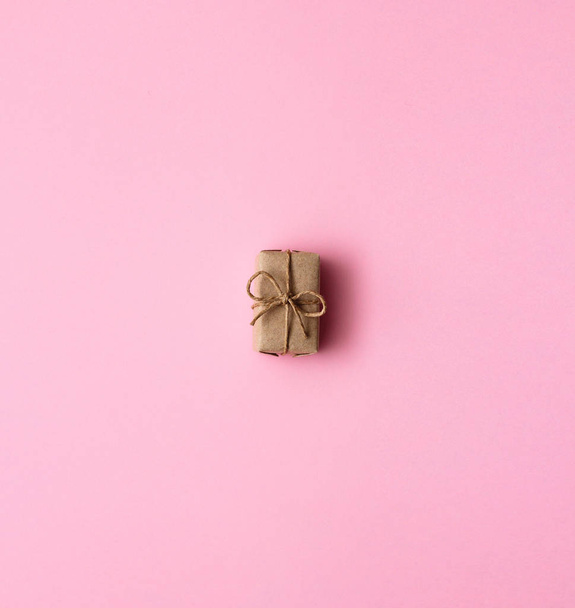 Single gift box wrapped in brown craft paper and tie hemp cord. Pink background.  - Fotó, kép